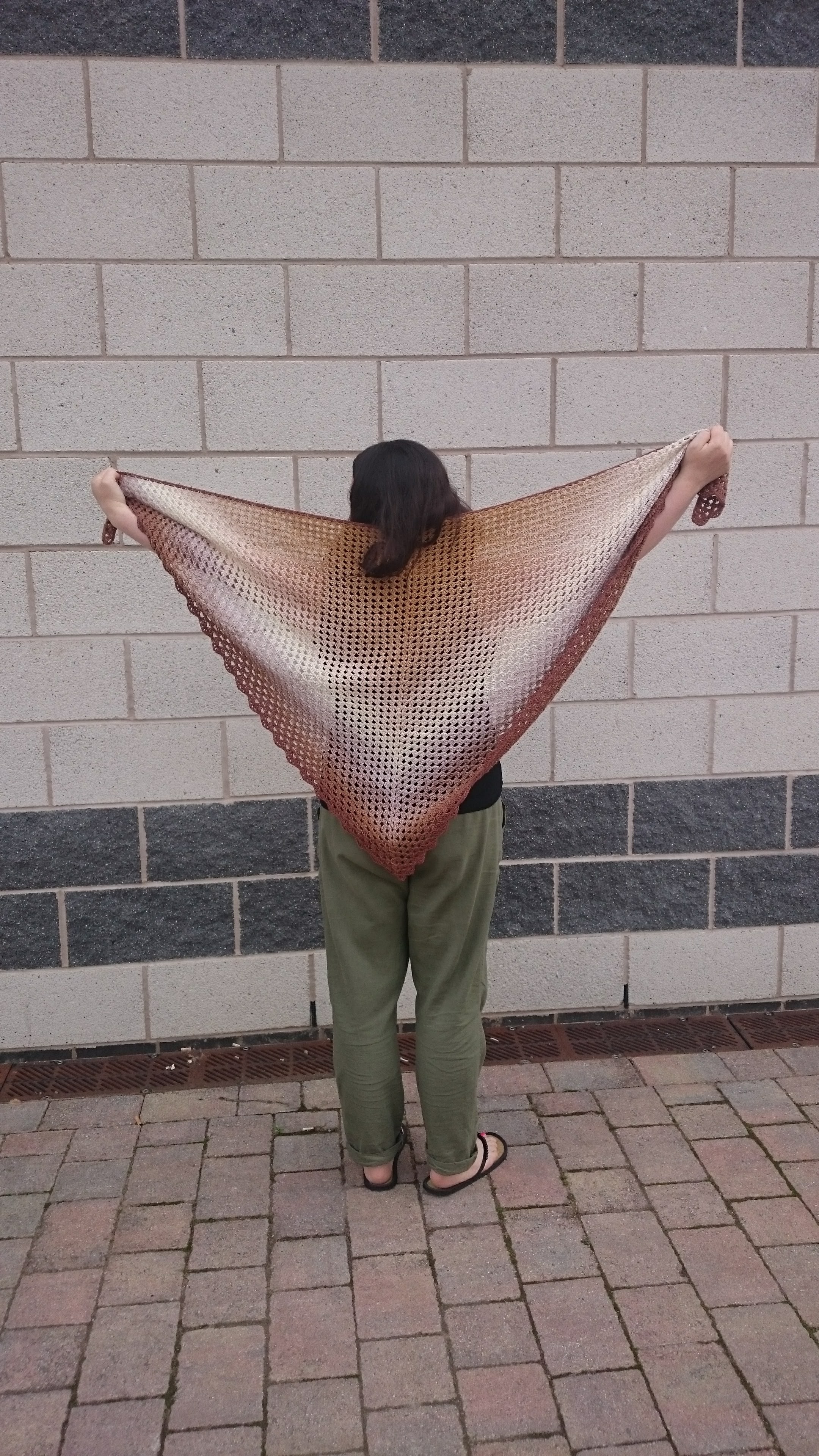 Female photographed from the back holding up a brown crocheted shawl for the camera to see