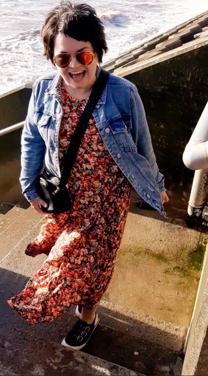 Female being windswept on beach steps wearing red dress and blue denim jacket